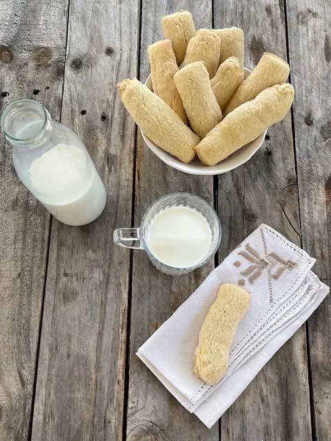 la foto mostra una ciotola con i biscotti e in primo piano un bel biscotto da inzuppo con una tazza di latte accanto