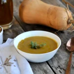 Un piatto di vellutata di zucca e ceci Bimby cremosa e con rosmarino e altri ingredienti intorno